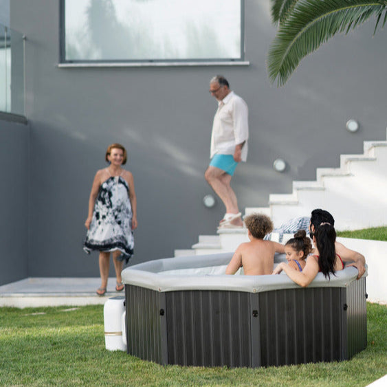 Family enjoying a hot tub in a modern outdoor setting with a house and palm tree in the background.