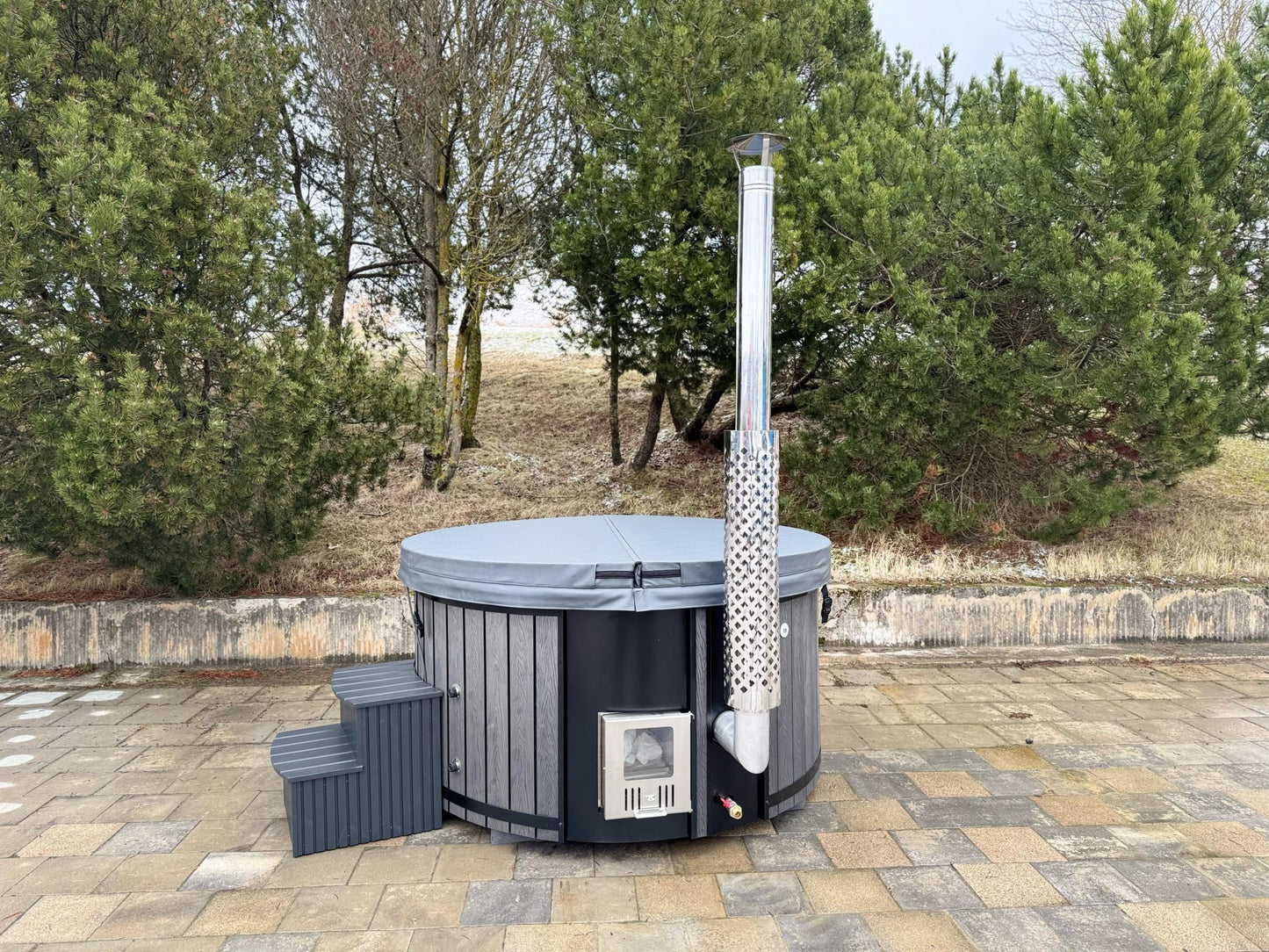 Hot tub with a chimney-like structure outdoors on a paved area with trees in the background