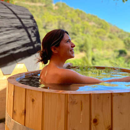 Woman in a wooden hot tub with a scenic background of trees and mountains.